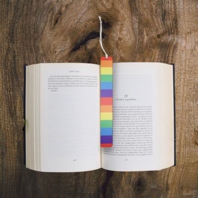 Livro aberto com marcador de páginas arco-íris numa mesa de madeira