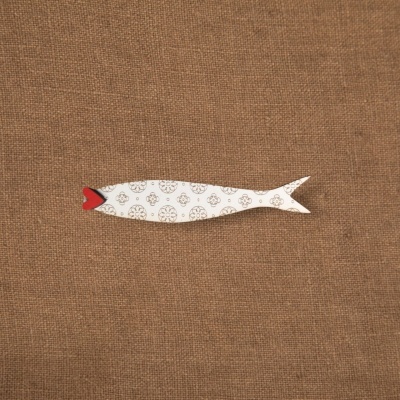 Peixe decorativo em madeira branca com padrões castanhos e boca vermelha sobre tecido castanho