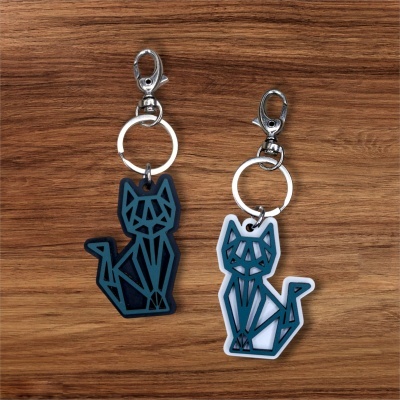 Dois porta-chaves com pingentes de gato geométricos em preto e branco sobre fundo de madeira.