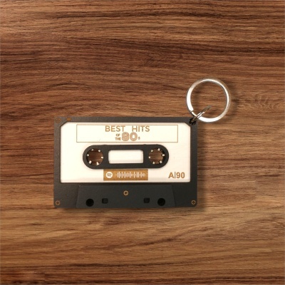 Chaveiro em forma de cassete de áudio preto, branco e bege sobre superfície de madeira