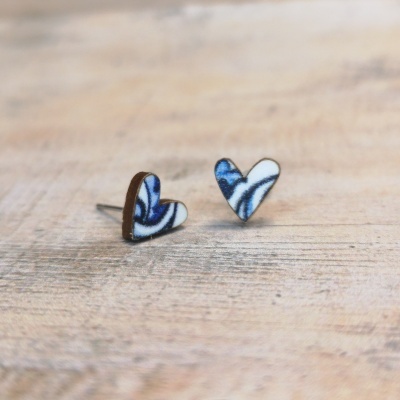 Brincos em forma de coração com padrão azul e branco sobre fundo de madeira clara.