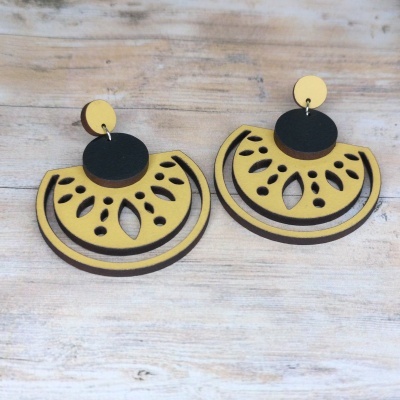 Brincos em madeira cortada laser amarelo e preto em superfície de madeira.