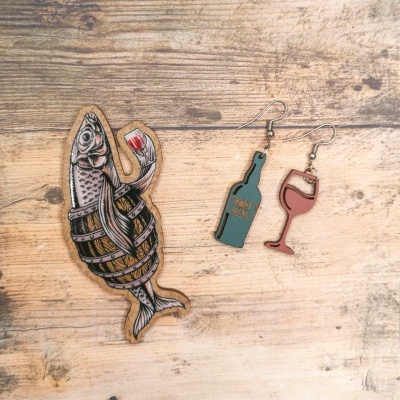 Broche peixe com copo de vinho e brincos garrafa e copo de vinho sobre mesa de madeira