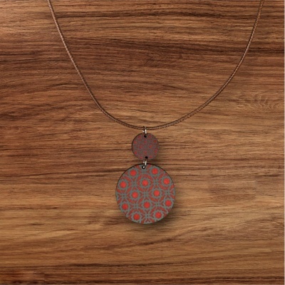 Colar com pendente duplo redondo com padrão geométrico vermelho e cinza num fundo de madeira