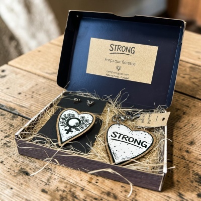 Conjunto de acessórios de madeira em forma de coração com símbolos femininos e texto STRONG, numa caixa azul