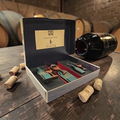 Caixa aberta com prendas em forma de garrafa e copo de vinho, texto Port Wine, garrafas e rolhas numa mesa de madeira