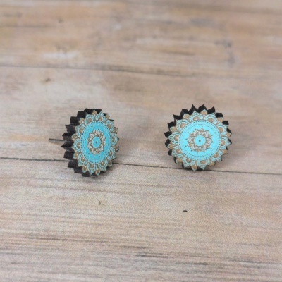 Brincos de madeira redondos com desenho mandala azul e castanho em fundo de madeira.