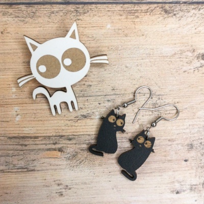 Brincos de gato pretos em madeira com fechos metálicos sobre mesa de madeira clara