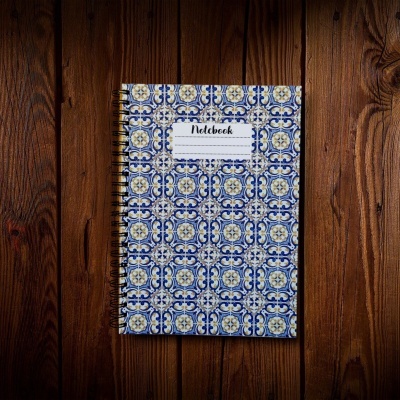 Caderno com capa decorada com padrão de azulejos azul e amarelo e etiqueta 'Notebook' em mesa de madeira.