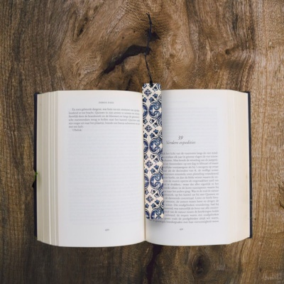 Livro aberto com marcador de páginas estampado azul e branco sobre mesa de madeira