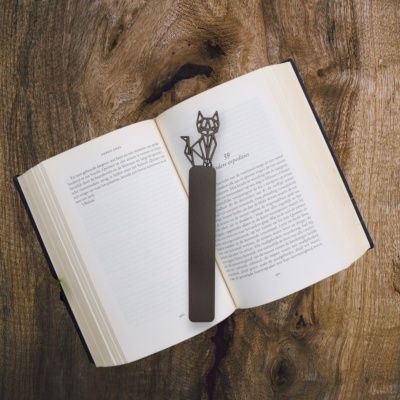 Marcador de livros metálico com figura de gato num livro aberto sobre madeira