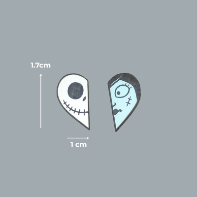 Dois pendentes pequenos em forma de gotas, branco com caveira e azul com rosto, medindo 1,7 cm por 1 cm, fundo cinza.