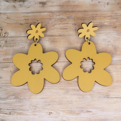 Brincos amarelos em forma de flores sobre superfície de madeira clara