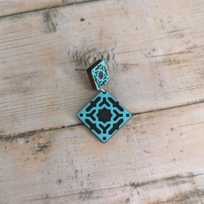 Brinco de madeira azul e preto com padrão geométrico sobre mesa de madeira clara