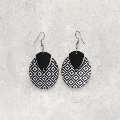 Brincos pretos e brancos com padrão geométrico sobre fundo cinzento.