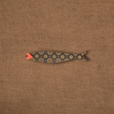 Peixe decorativo em madeira pintada com padrões dourados e lábio vermelho sobre fundo castanho.