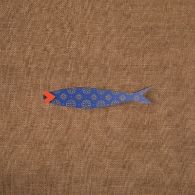 Peixe decorativo azul com padrão dourado e boca vermelha sobre tecido castanho.