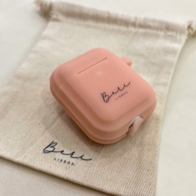 Estojo cor-de-rosa para AirPods sobre saco de tecido com texto Belle AIRPods