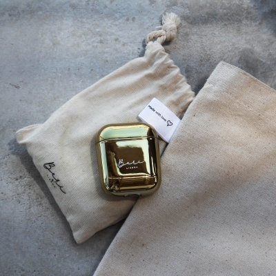 Estojo dourado para auriculares com saco de tecido cru sobre superfície cinzenta.