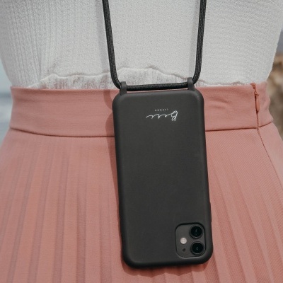 Capa preta de telemóvel com alça de pescoço pendurada em roupa clara junto à praia