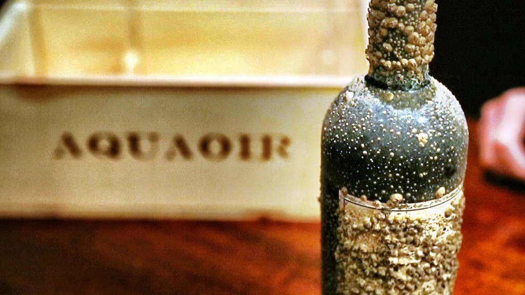 frasco escuro com material granulado ao lado de caixa com texto AQUAOIR