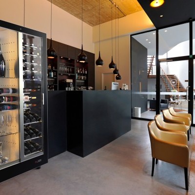 Frigorífico de vinho preto com vidro, garrafas e copos num espaço moderno com cadeiras amarelas