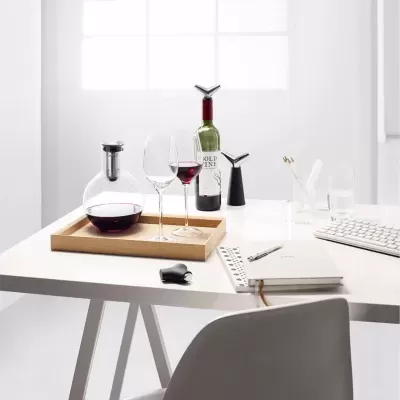 Mesa branca com decantador, taças, garrafa de vinho, caderno, teclado e acessórios
