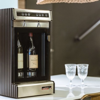 Refrigerador de vinho preto com duas garrafas e dois copos de vidro sobre mesa branca