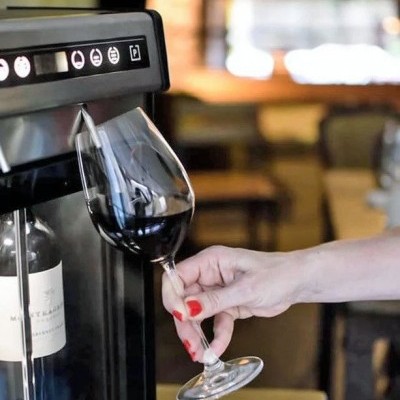 Máquina automática a servir vinho tinto em taça de vidro com mão feminina segurando