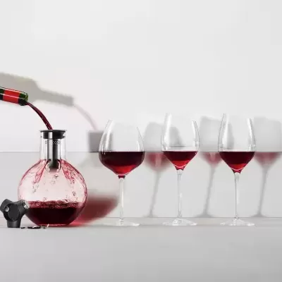 Vinho a ser vertido numa garrafa redonda com quatro copos de vinho alinhados
