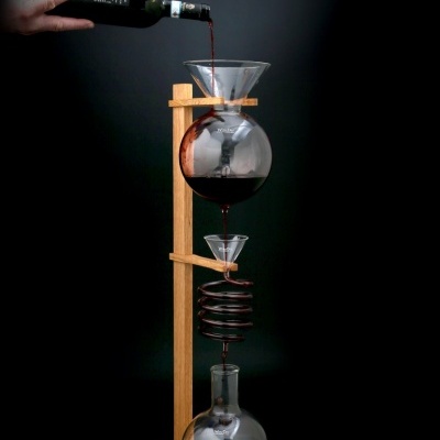 Dispositivo de vidro para decantação de vinho com suporte de madeira e garrafa preta a verter vinho.