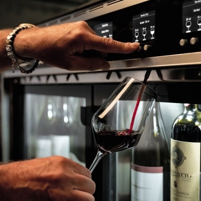 Máquina dispenser de vinho com ecrãs digitais e taça a ser preenchida com vinho tinto