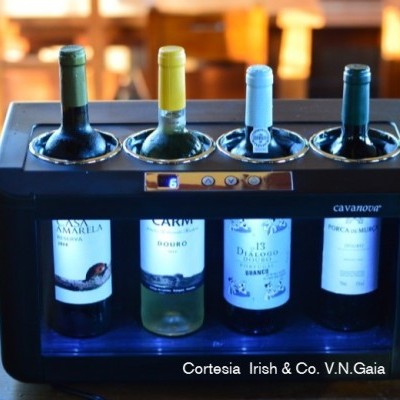 Máquina dispensadora de vinho com quatro garrafas diferentes em caixa preta sobre mesa de madeira