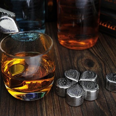 Copo com bebida âmbar e pedras metálicas sobre mesa de madeira