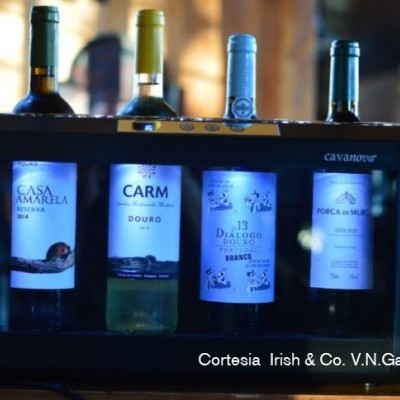 Quatro garrafas de vinho em embalagem preta iluminada com etiquetas visíveis.