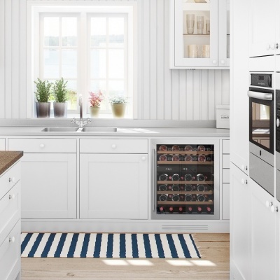 Cozinha branca moderna com adega embutida cheia de vinhos e janela com plantas