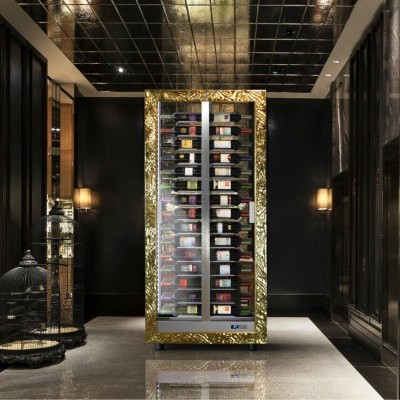 Adega climatizada dourada com garrafas de vinho visíveis num corredor escuro