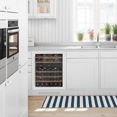 Cozinha branca moderna com adega para vinhos, forno duplo, bancada e plantas no peitoril da janela