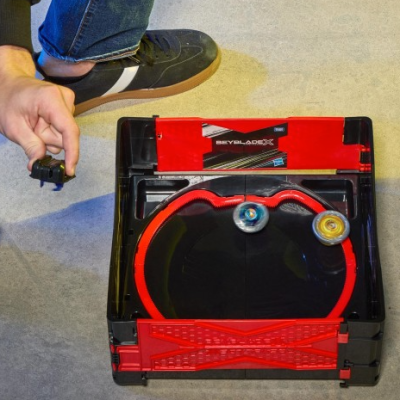 Beyblade battle arena with two tops spinning and person holding launcher