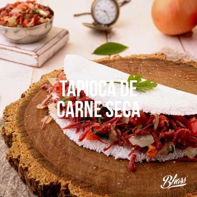 Tapioca de carne seca com carne e cebola numa mesa de madeira