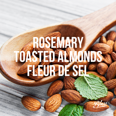 Amêndoas torradas com alecrim e flor de sal numa colher de madeira com folhas verdes ao lado.