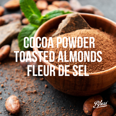 Recipiente de madeira com cacau em pó e amêndoas torradas em fundo escuro com texto sobreposto.