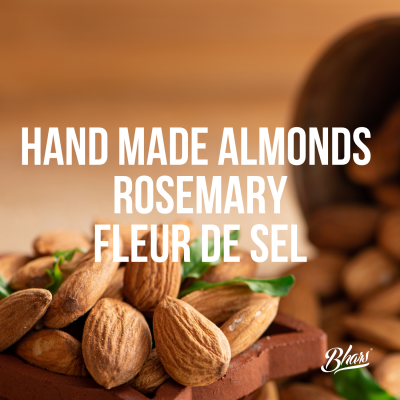 Amêndoas naturais com texto 'HAND MADE ALMONDS ROSEMARY FLEUR DE SEL' e saco de pano ao fundo