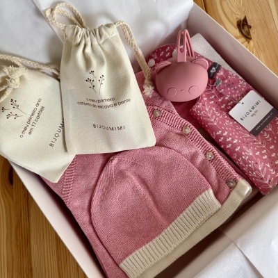 Kit presente com roupas e acessórios rosa e branco, bolsas de tecido com textos em português, etiqueta BIJOUMIMI baby gift, caixa branca em mesa de madeira