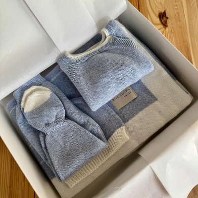 Conjunto de roupa de bebé azul e branca em caixa branca com papel de seda