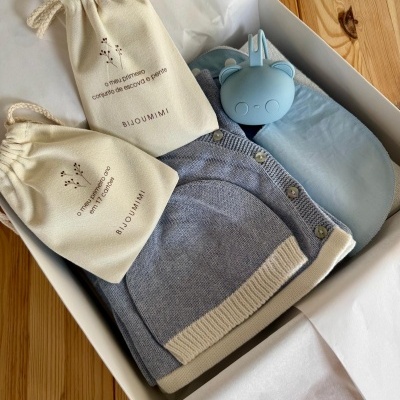 Caixa de presente com roupa de bebé, babete, biberão de silicone e sacos de algodão com texto em português