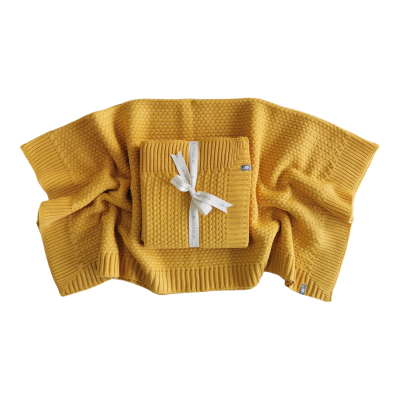 Mantas de malha amarelas com textura canelada e ponto de arroz, uma estendida e outra dobrada com fita branca.