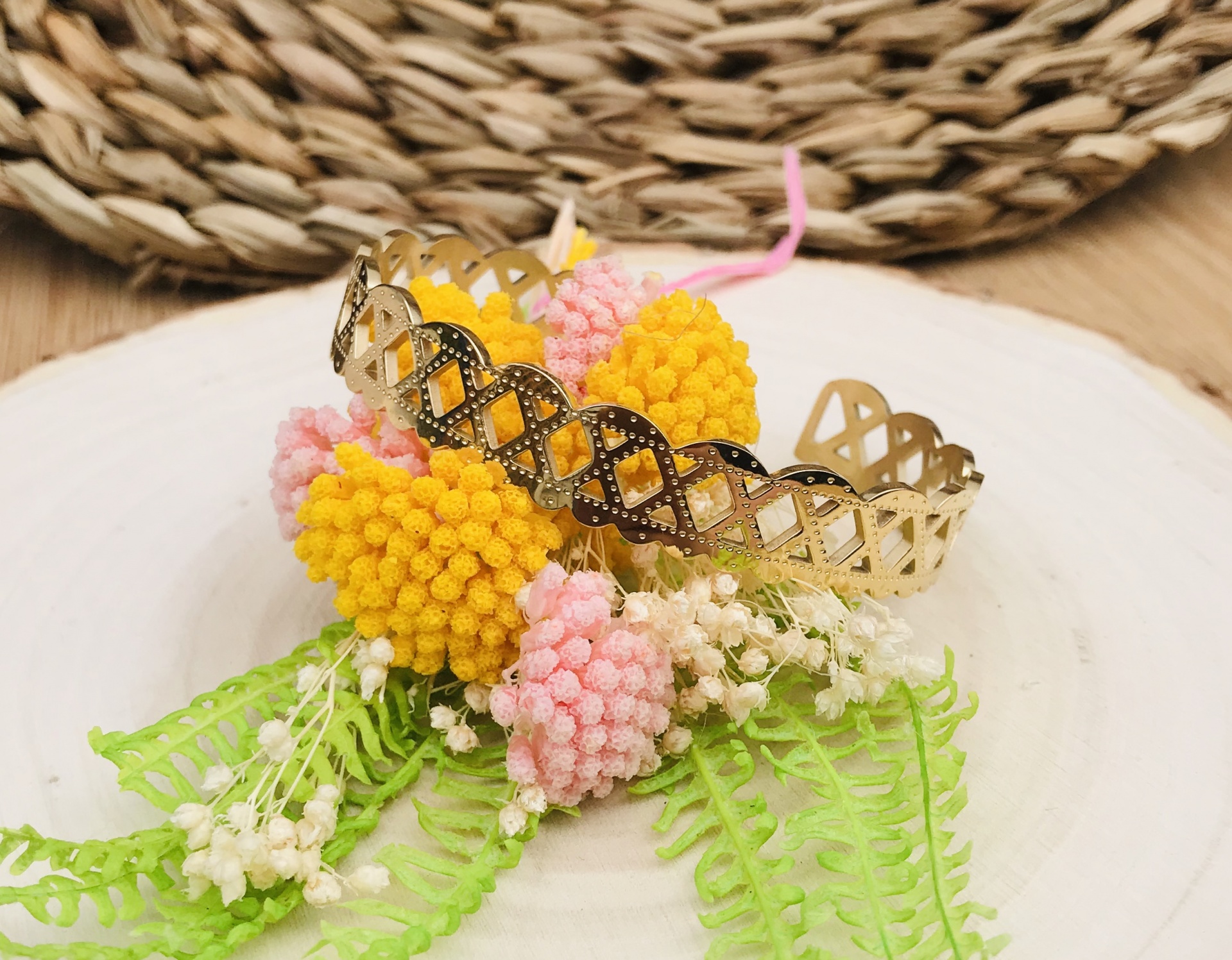 Pulseira dourada com flores decorativas amarelas e rosa sobre prato branco