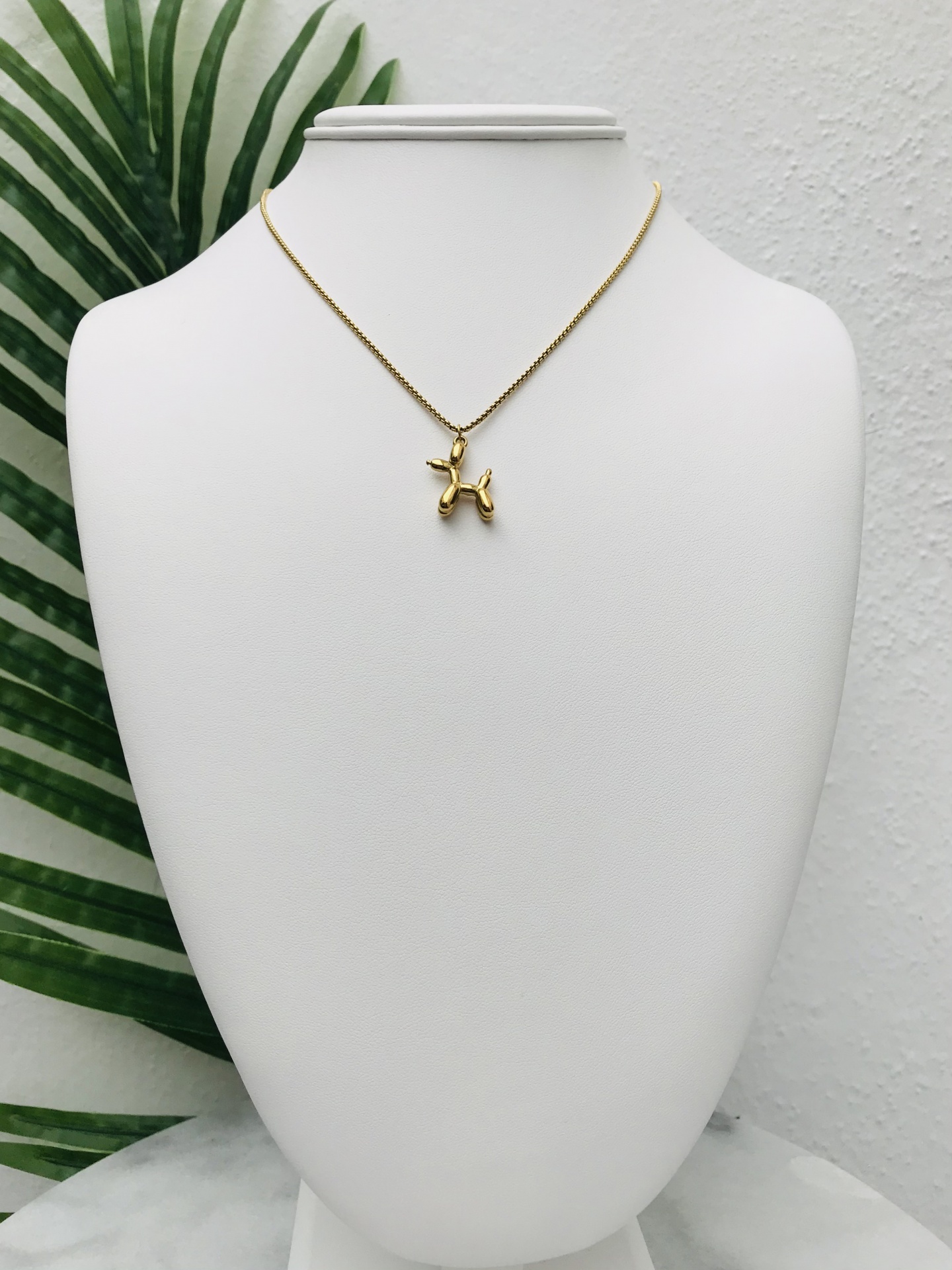 Colar dourado com pendente em forma de balão de animal num busto branco