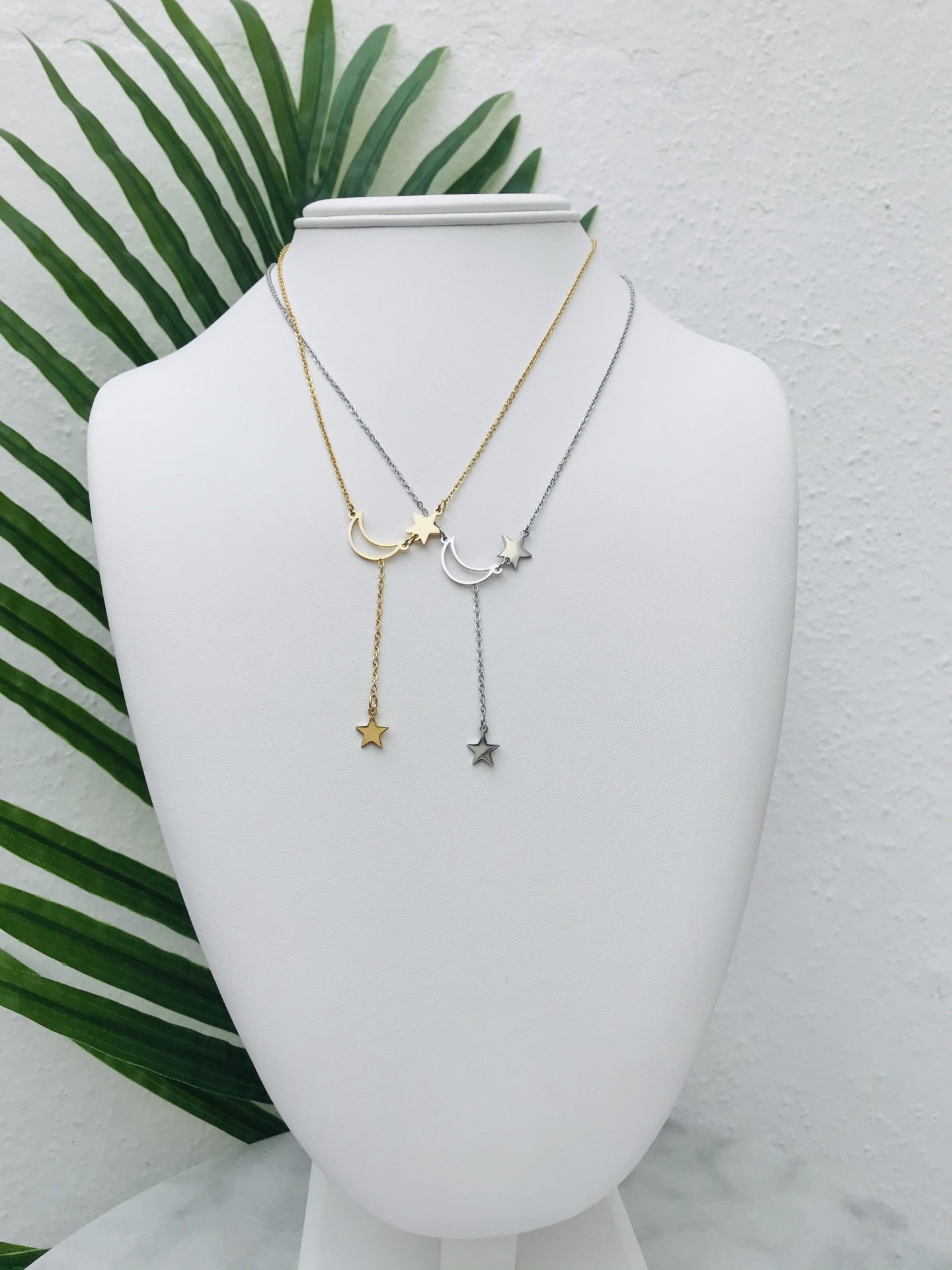 Colares dourado e prateado com pendentes de lua e estrela em suporte branco
